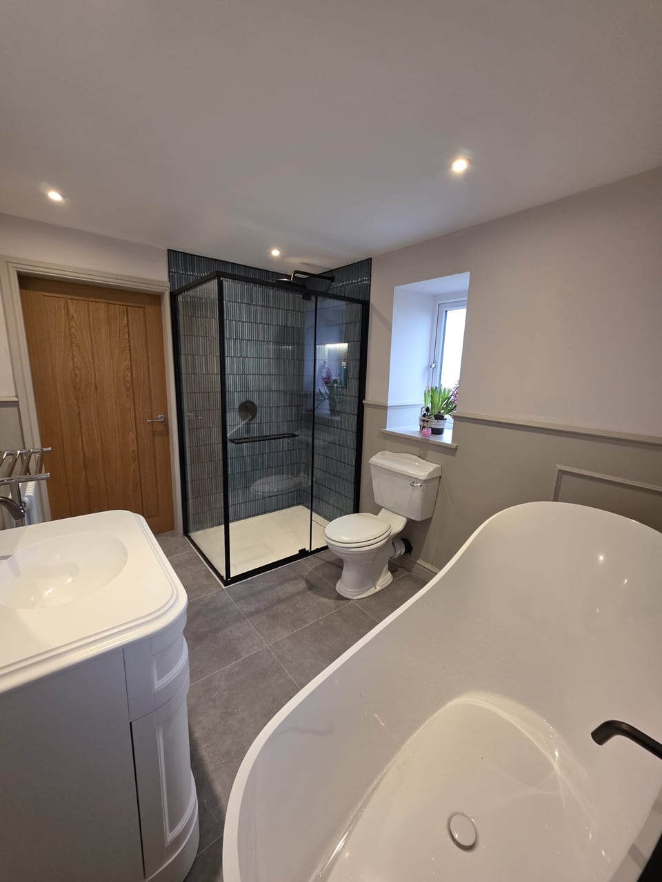 Finished bathroom with a black-framed ribbed-glass shower, white freestanding bath, vanity unit and toilet