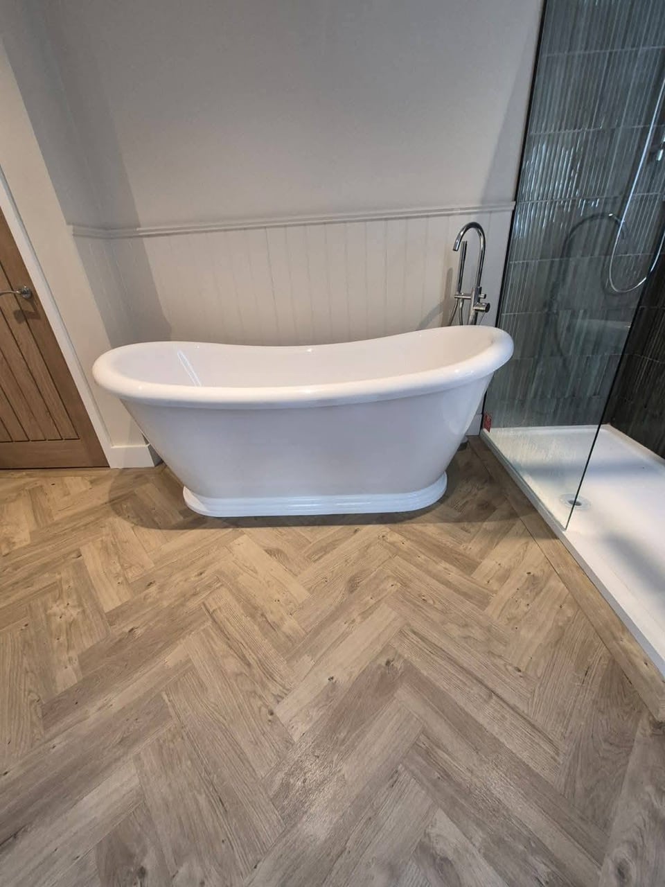 White freestanding bath beside a glass shower with dark vertical tiles