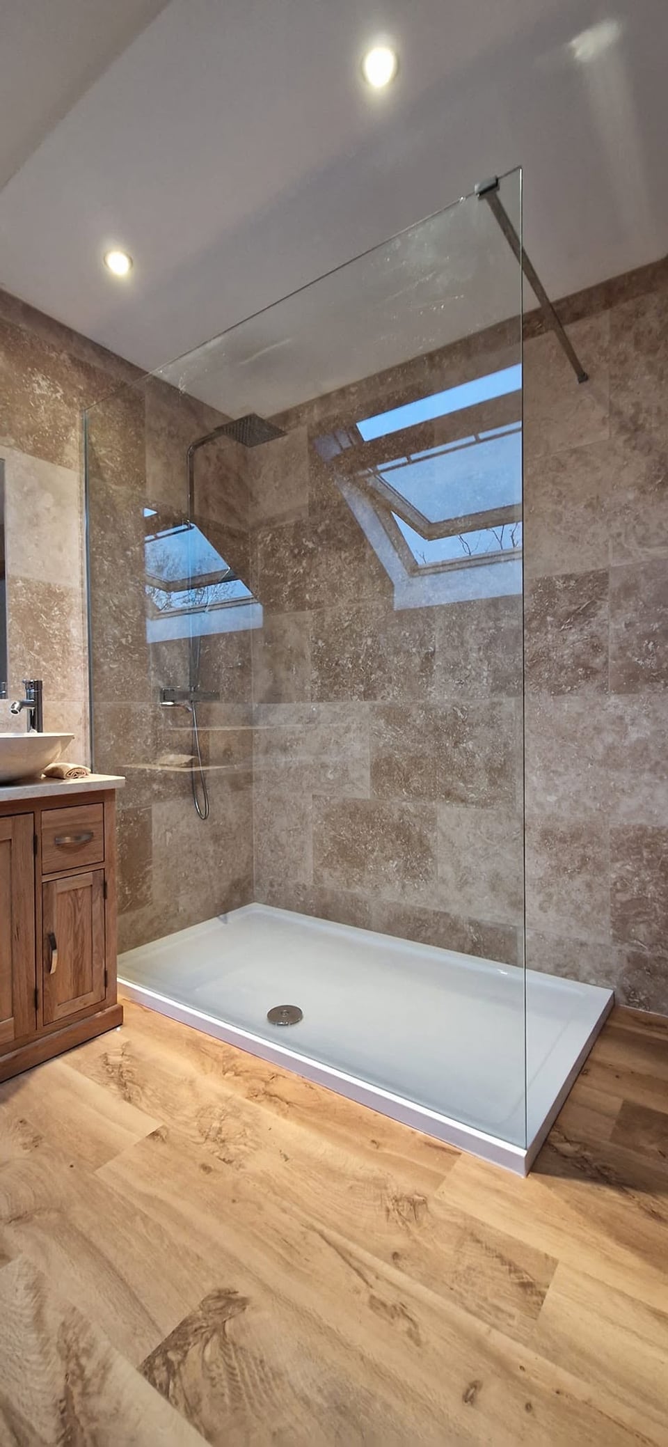 Large shower with a frameless glass screen, square rainfall head and brown stone-effect tiles
