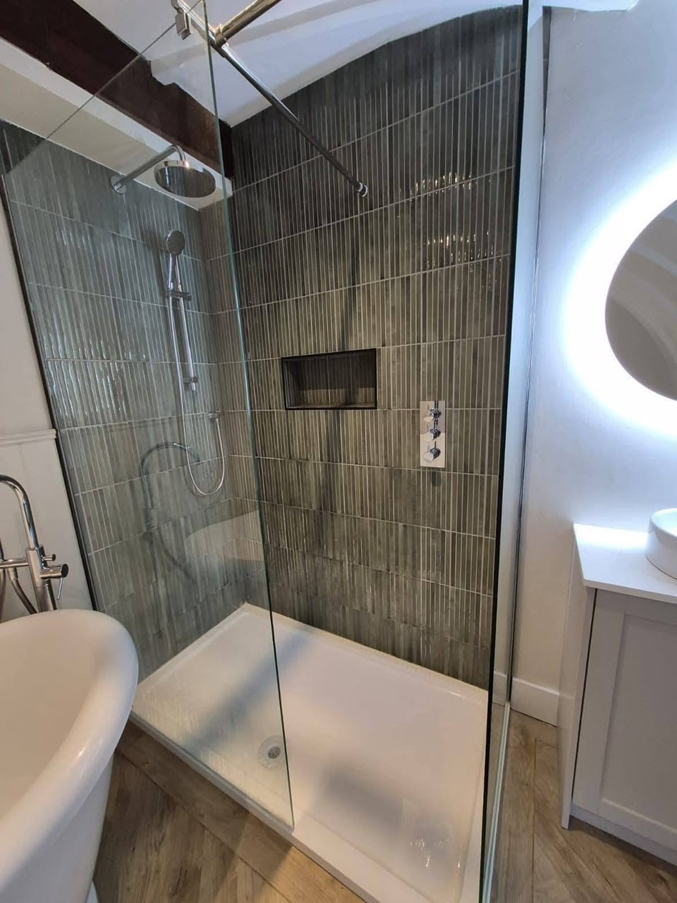 Glass shower enclosure with dark vertical tiles, rainfall shower and recessed shelf