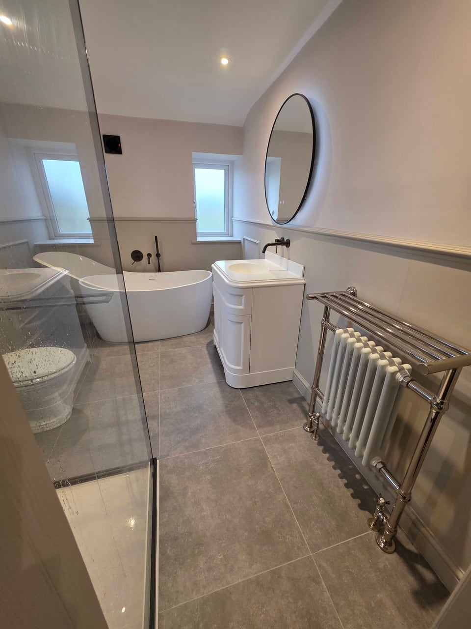 Bathroom with a white freestanding bath, vanity unit and chrome column radiator