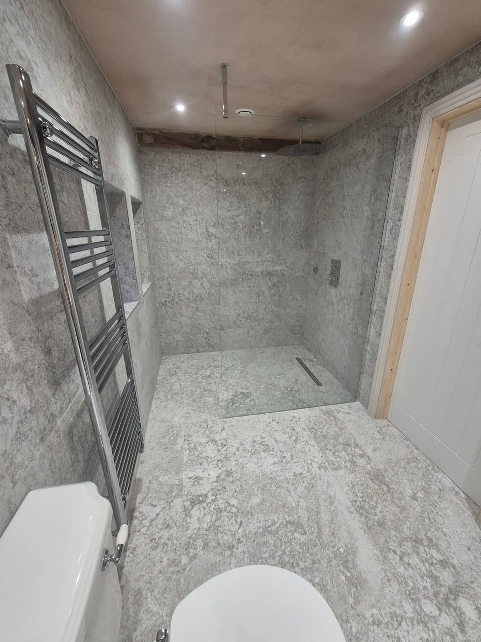Grey stone-effect shower area with glass screen, recessed shelves and chrome towel rail