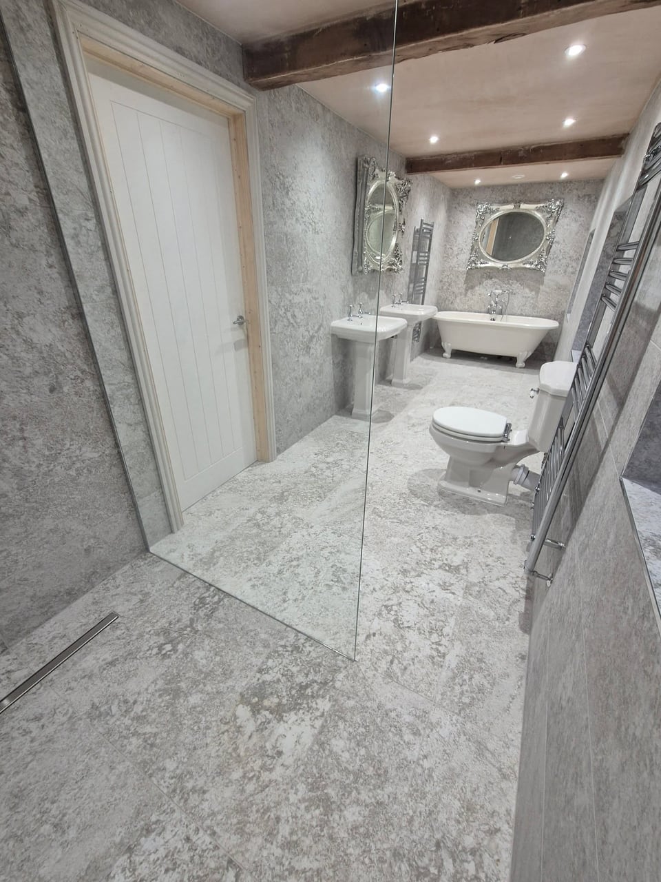 Grey bathroom with an open shower screen, two pedestal basins, toilet and roll-top bath