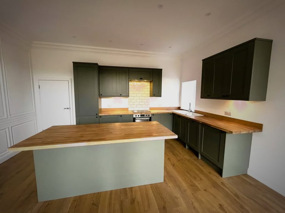 Kitchen with dark green cabinets, timber worktops and a central island