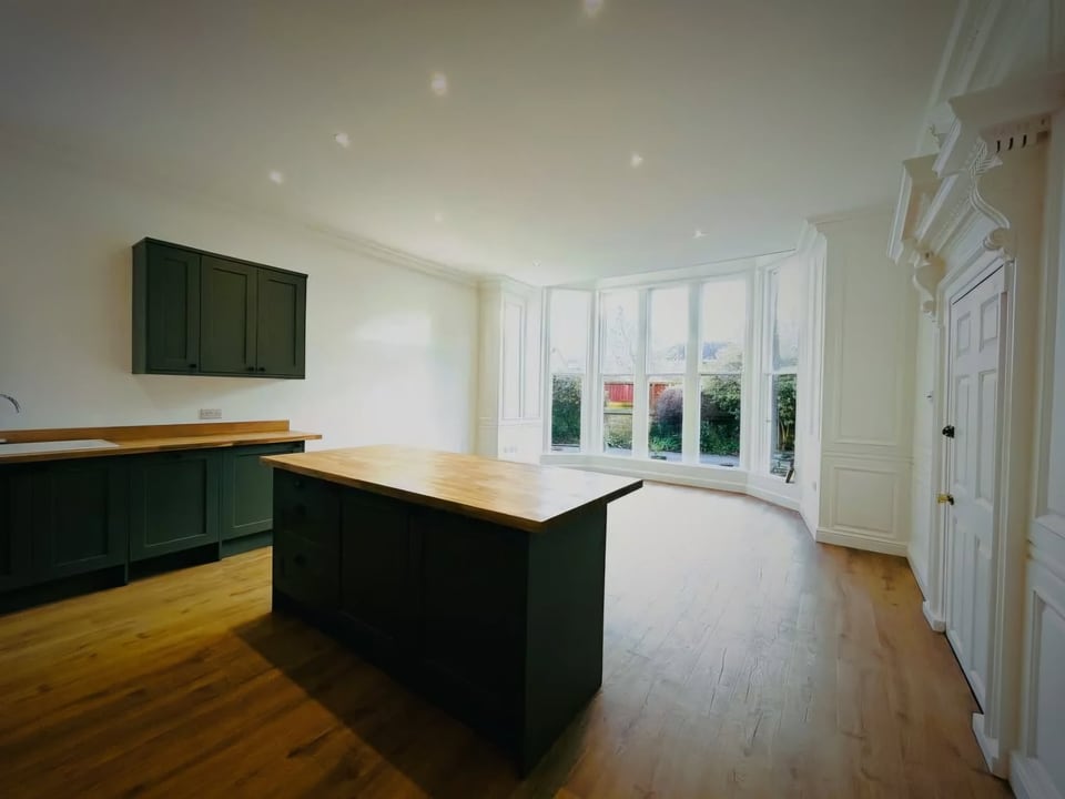 Dark green kitchen island and cabinets in a room with a large bay window